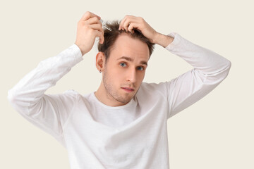 Young man using serum for hair growth on white background