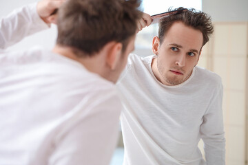 Young man combing hair near mirror in bathroom