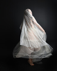 Fototapeta na wymiar Full length portrait of beautiful woman wearing white gown dress with flowing ghostly veiled fabric, isolated on dark studio background.