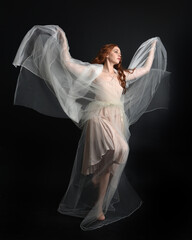 Full length portrait of beautiful woman wearing white gown dress with flowing ghostly veiled fabric, isolated on dark studio background.