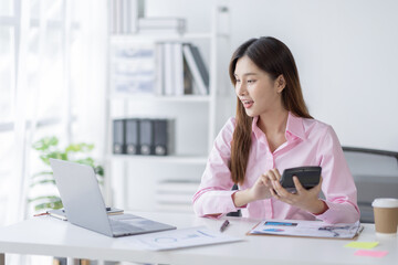 Asian Businesswoman Using laptop computer and working at office with calculator document on desk, doing planning analyzing the financial report, business plan investment, finance analysis concept.
