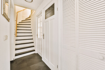 a hallway with white walls and black tile on the floor, leading up to an open door that leads to a...