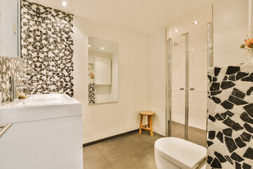 a modern bathroom with black and white tiles on the walls, toilet, sink, and shower stall in it