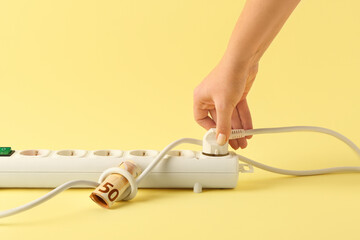 Woman inserting plug with money into power socket on yellow background. Electricity bill concept