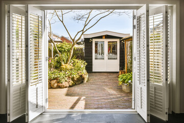 an open front door with shutters on the outside and trees in the yard behind it, as seen from inside