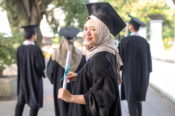 Smiling young Muslim female graduate, standing with a diploma in hand and looking at the camera.  Education, graduation and people concept.