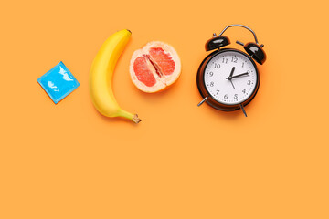 Banana with grapefruit, condom and alarm clock on orange background. Sex concept