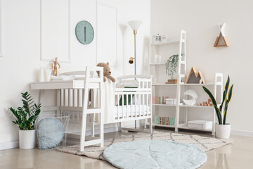Interior of light bedroom with baby crib, changing table and shelving unit