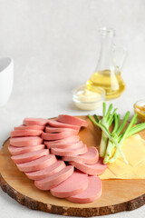 Wooden board with tasty sliced boiled sausage and cheese on light background