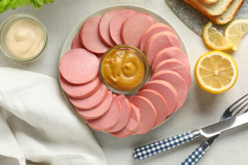 Plate with tasty sliced boiled sausage and sauces on light background