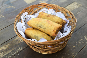 Banana rolls served in bamboo basket upon wooden table