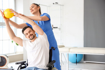 Female physiotherapist working with young man in wheelchair at rehabilitation center