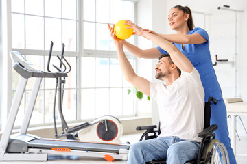 Female physiotherapist working with young man in wheelchair at rehabilitation center