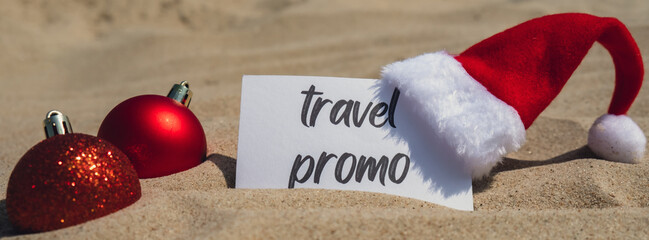 TRAVEL PROMO text on paper greeting card on background sandy beach sun coast. Christmas balls Santa hat New Year New Me decoration. Summer vacation decor. Holiday concept calendar date postcard