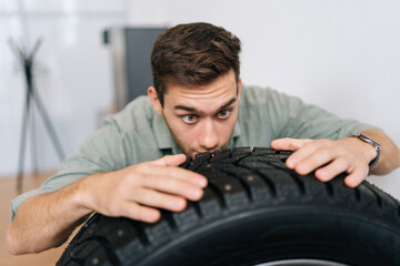 Portrait of funny young man customer examining brand and product characteristics while buying new tires in auto department of dealership. Male client choosing car accessories in shopping mall.