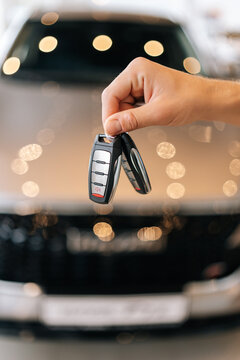 Vertical closeup cropped shot of unrecognizable buyer male holding in hand car key from new auto after buying at showroom on blurred background of new auto. Concept of choosing and buying new car.