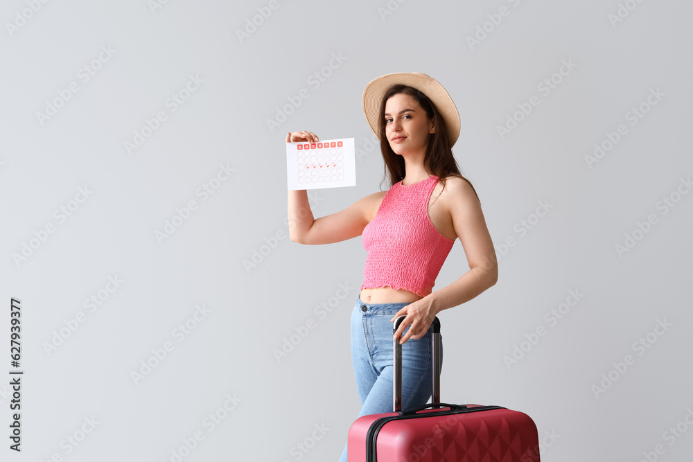 Wall mural young woman with menstrual calendar and suitcase on light background