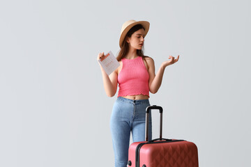 Young woman with menstrual calendar and suitcase counting on light background