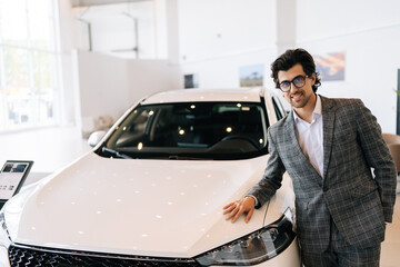 Portrait of confident customer male in business suit touching hood of new car standing looking at...
