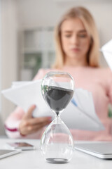Hourglass on table of businesswoman in office, closeup. Deadline concept