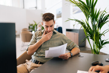 Portrait of focused male client reading contract for real estate property purchase. Thoughtful man reading terms of conditions of document, making decision about house purchase or financial investment - obrazy, fototapety, plakaty