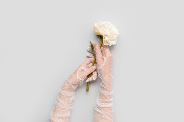 Female hands in laced gloves with beautiful peony flower on light background