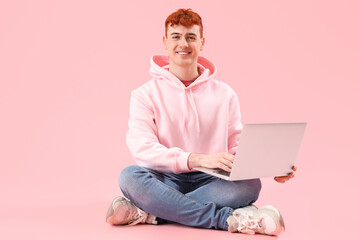 Young redhead man using laptop on pink background