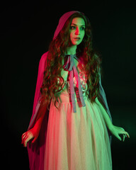 Close up  portrait of beautiful brunette woman wearing  a gown with purple fantasy cloak, posing with arms reaching out. isolated on dark studio background with cinematic colourful lighting.