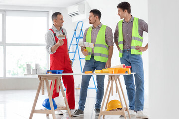 Team of male builders with paint rollers working in room
