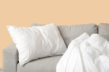 Fototapeta na wymiar Grey sofa with white pillow and blanket near beige wall