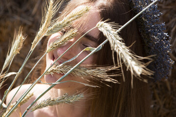 Portrait of a young beautiful woman with spikelets of wheat in a wreath of lavender flowers.