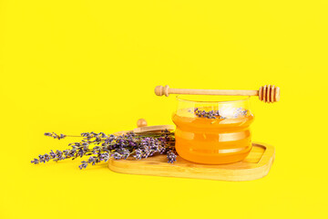 Wooden board with jar of sweet lavender honey, dipper and flowers on yellow background