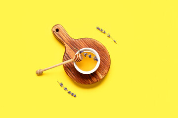 Wooden board with bowl of sweet lavender honey, dipper and flowers on yellow background