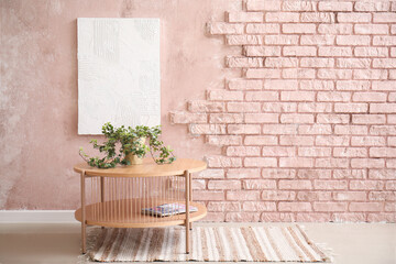 Wooden coffee table with houseplant in room near pink brick wall