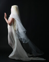 Fototapeta na wymiar Full length portrait of beautiful blonde woman wearing white gown dress with flowing ghostly veiled fabric, isolated on dar studio background.