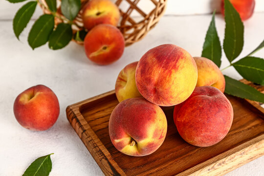 Wooden board with sweet peaches and leaves on white table