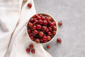 Bowl with fresh gooseberries on grey background