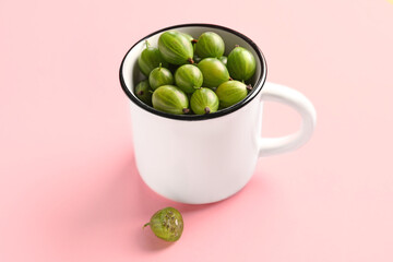 Cup with fresh gooseberries on pink background