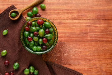 Bowl with fresh gooseberries on wooden background