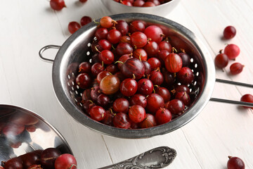 Colander with fresh gooseberries on white wooden background
