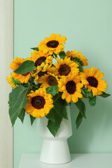 Vase with beautiful sunflowers on white table near green wall