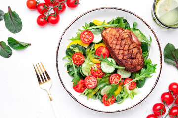 Salad with grilled duck breast and cherry tomatoes, cucumber, paprika, lettuce and arugula on white table background, top view