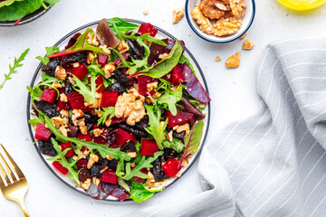 Healthy vegan salad with beet, dry prunes, arugula, swiss chard and walnuts, white table background. Fresh useful vegetarian dish for clean eating