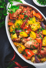 Turkey roast with potatoes, paprika, red onions, parsley and spices in baking dish, black table background, top view