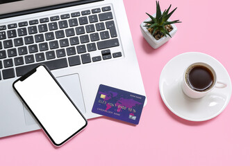 Laptop with credit card, cup of coffee and mobile phone on pink background