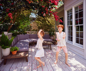 happy redhead kids, siblings having fun dancing on wooden terrace in summer garden at home