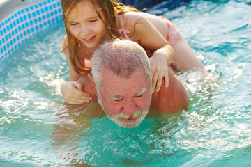 Grandpa and granddaughter play and have fun in the pool. 