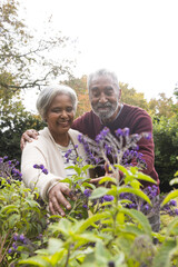 Happy senior biracial couple looking at flowers in garden at home, copy space