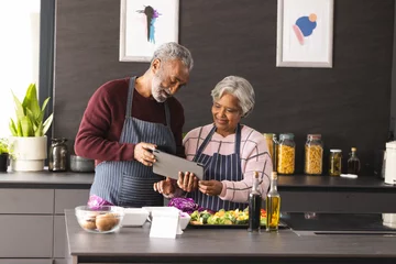  Happy senior biracial couple in aprons using tablet preparing vegetables in kitchen at home © WavebreakMediaMicro