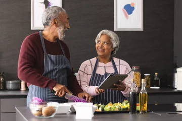  Happy senior biracial couple in aprons using tablet preparing vegetables in kitchen at home © WavebreakMediaMicro